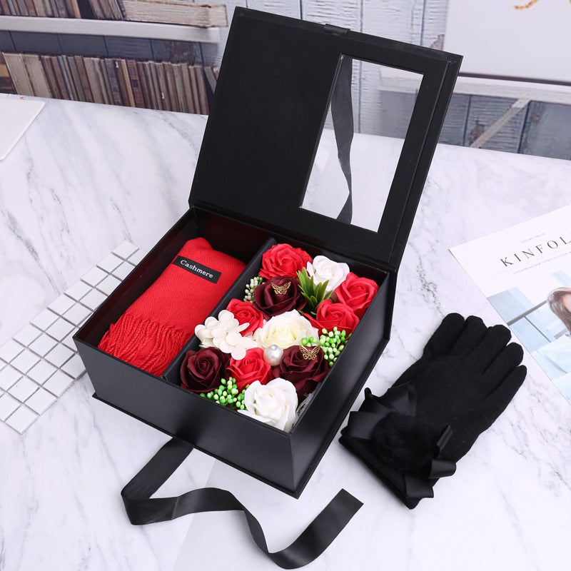 Black gift box with red scarf, flowers, and black gloves on a marble surface.