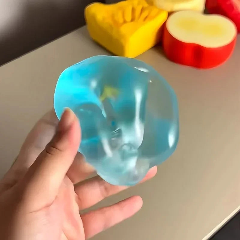 Hand holding a translucent blue maltose squishy stress toy, slow-rising sensory fidget with colorful foam shapes in the background, perfect for stress relief, anxiety reduction, and tactile sensory play.