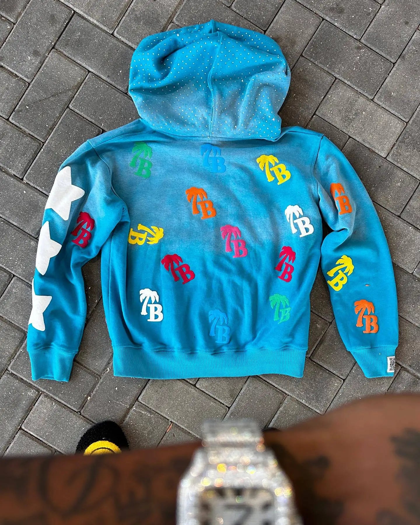 Blue hoodie with colorful logos on a tiled floor Blue hoodie with colorful logos on a tiled floor Blue hoodie with colorful logos on a tiled floor