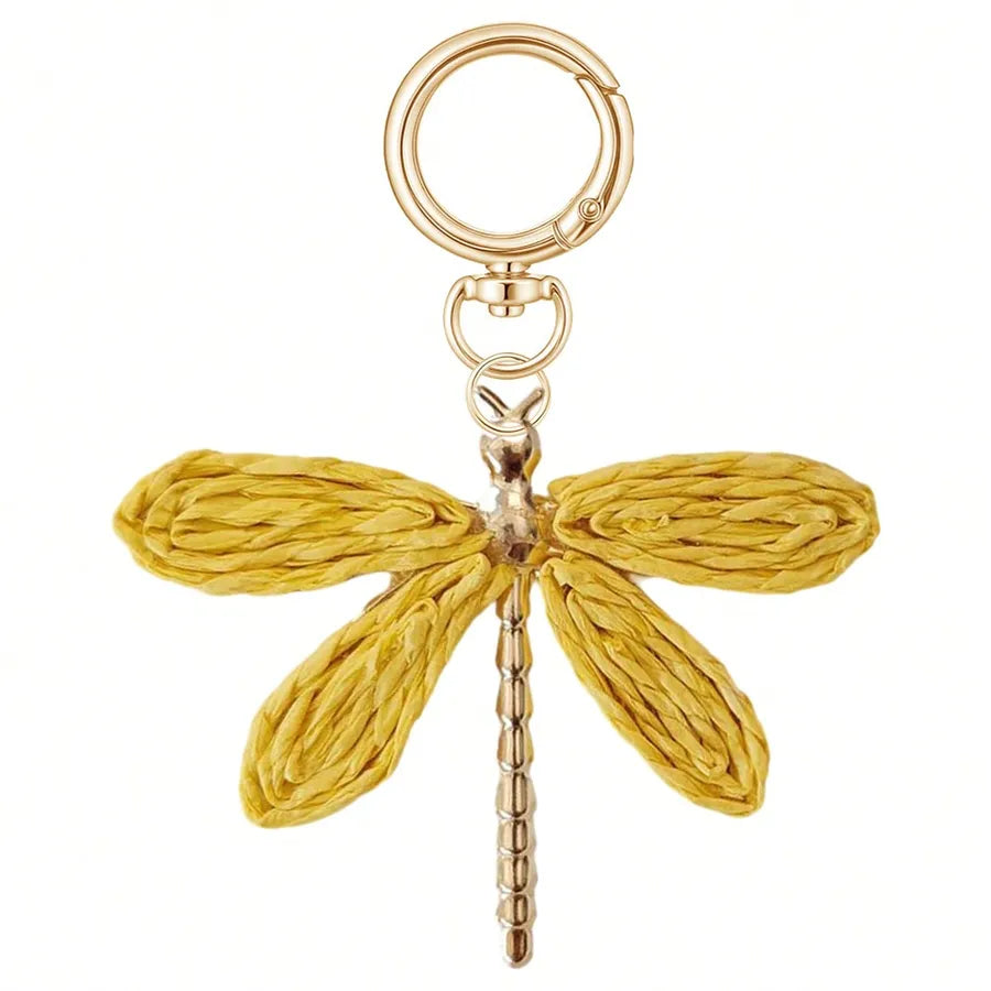 Golden yellow woven dragonfly bag charm with textured wings, gold-tone alloy body, and lobster clasp keyring, displayed on a white background. Decorative bohemian keychain accessory for handbags, purses, backpacks, and totes.