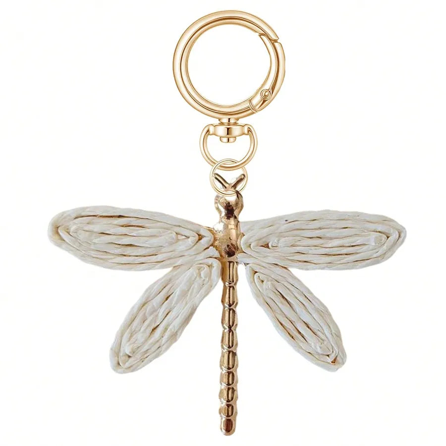 Gold and white dragonfly bag charm with woven-style wings and a polished gold-tone body, attached to a matching key ring on a white background. Bohemian alloy handbag accessory, purse charm, and decorative keychain.