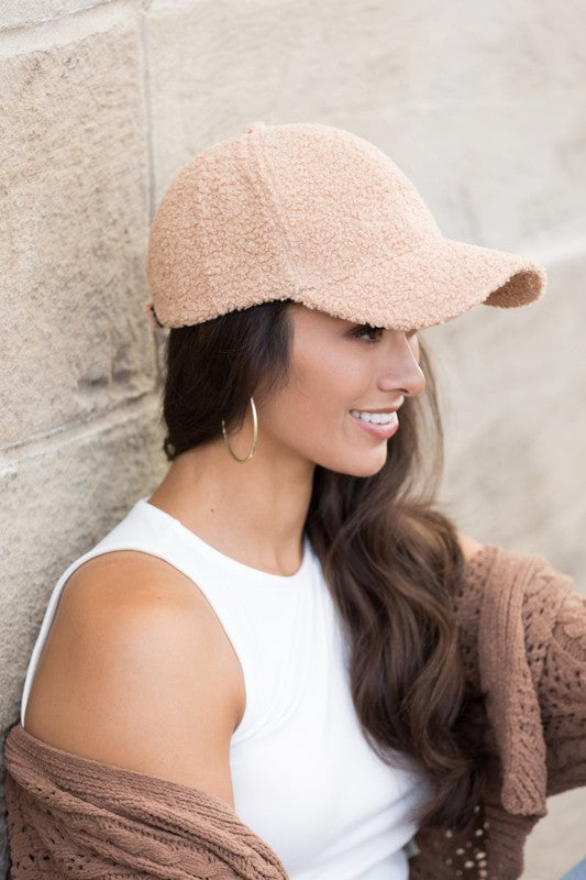 Woman wearing a beige cap and white top against a stone wall.