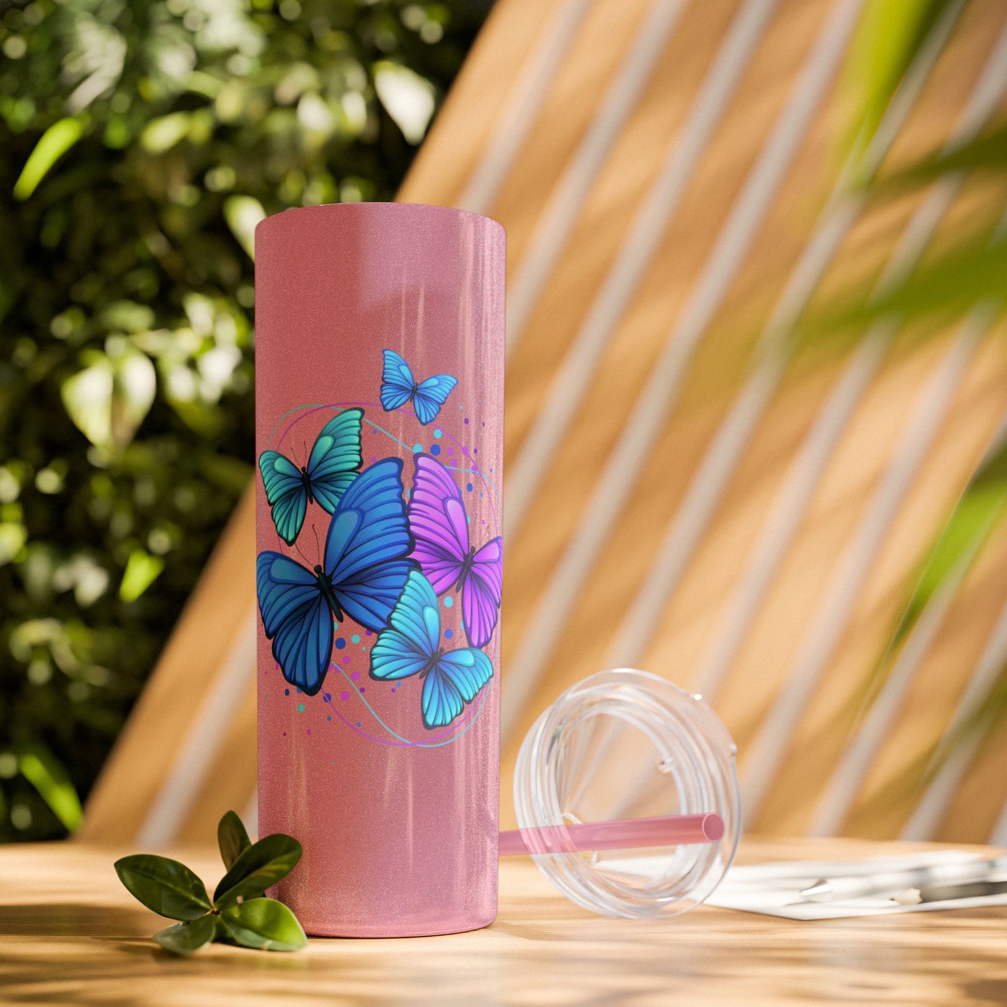 Pink tumbler with butterfly design on a wooden surface with a natural background