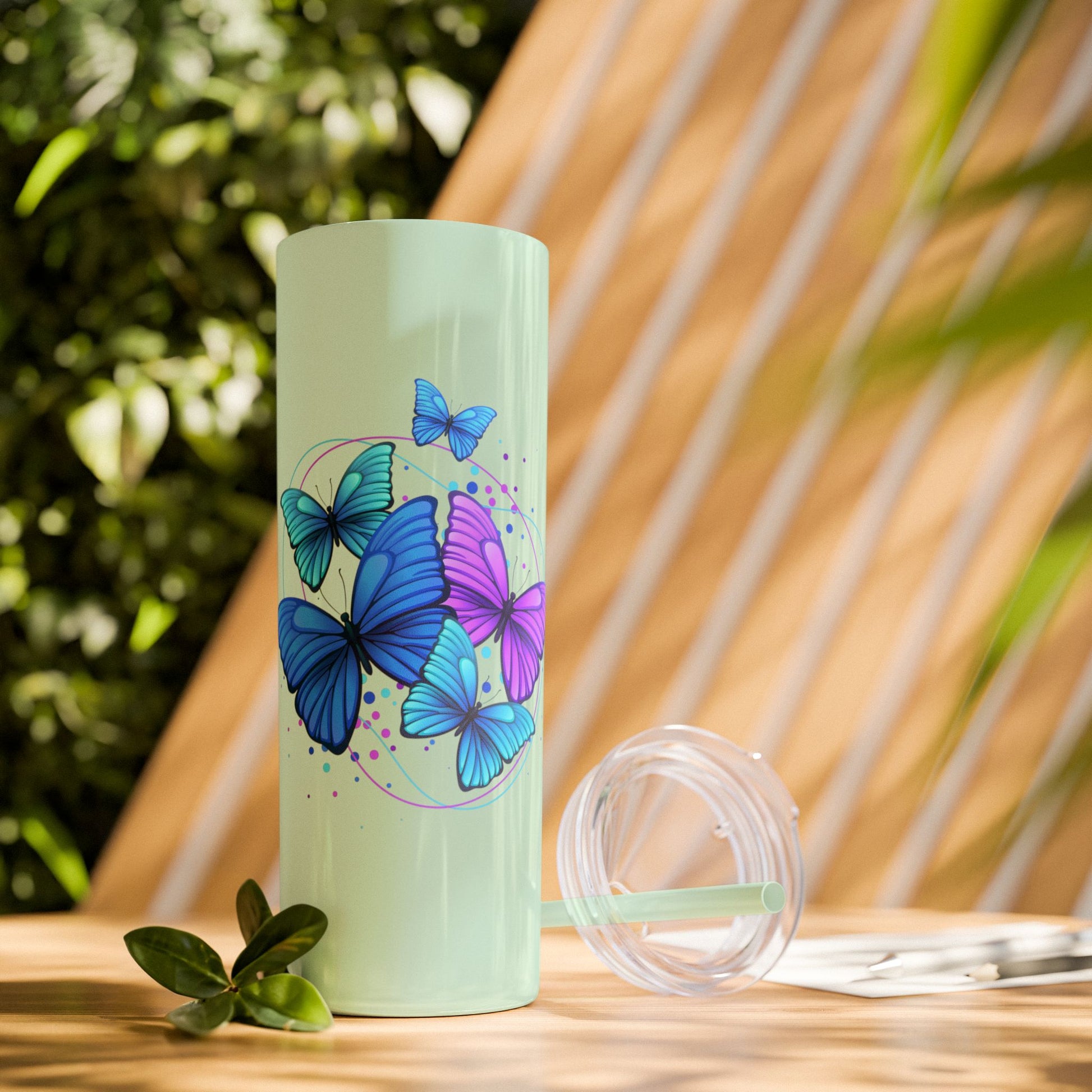 Mint green tumbler with butterfly design on a wooden surface with plants in the background