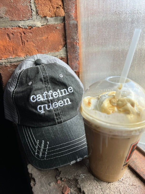 Cap labeled 'cafeine queen' next to a iced coffee drink on a brick surface. Caffeine Queen Trucker Hat 80% cotton/20% polyester, Herringbone fabric 100% polyester mesh back Velcro closure