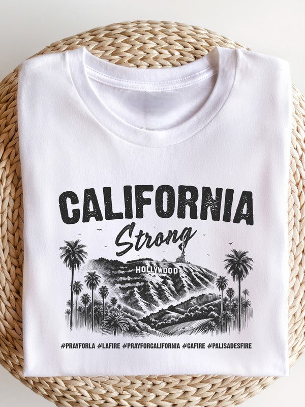 White unisex graphic T-shirt featuring the text "California Strong" with a vintage-style Hollywood hills and palm trees illustration, symbolizing Los Angeles pride and resilience.