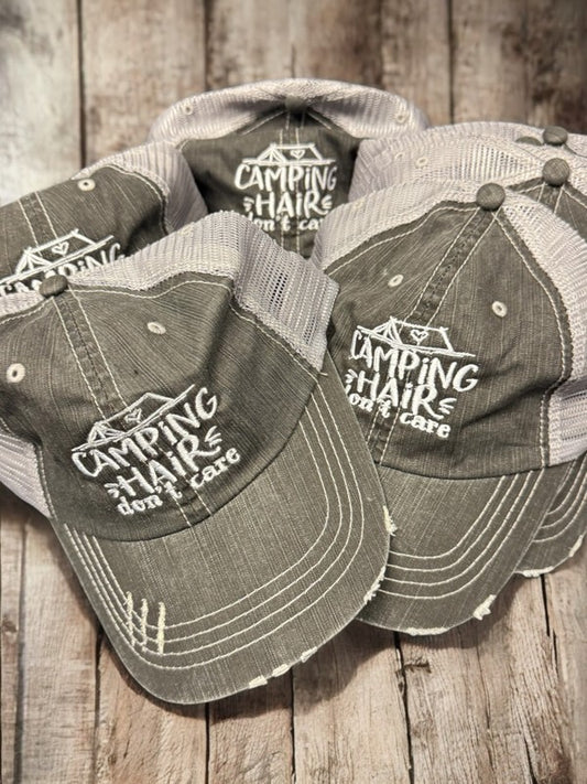 Three distressed hats with 'Camping Hairs Don't Care' text on a wooden surface. Camping Hair Don't Care Embroidered Trucker Hat – Funny Camping Cap for Women & Men, Adjustable Mesh Outdoor Adventure Hat