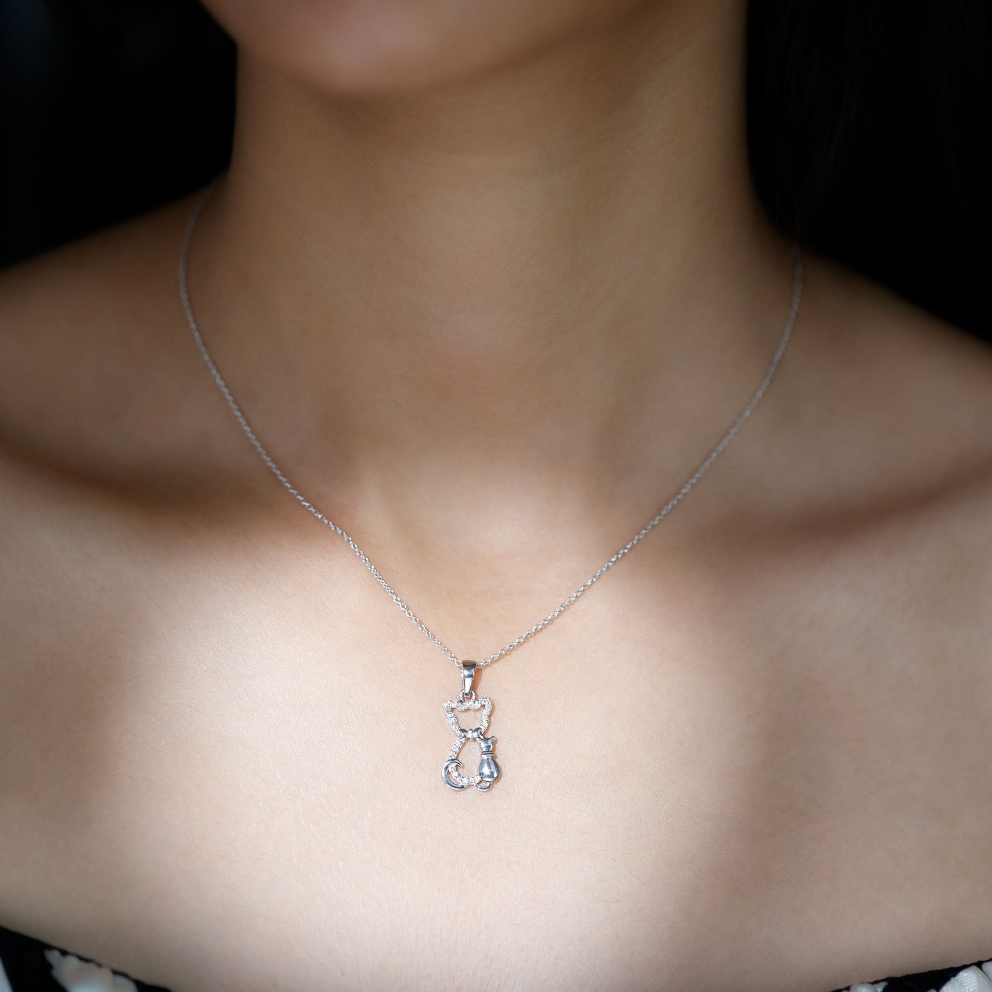 Silver necklace with a cat-shaped pendant on a person's neck against a dark background Kitty Cat Necklace, Cat Pendant, Cat Lover Gift, Diamond Necklace, Diamond Pendant, Lab Diamond Necklace, Natural Diamond Necklace, Fine Jewelry, Luxury Jewelry, Sterling Silver Necklace, 10K Gold Necklace, 14K Gold Necklace, 18K Gold Necklace, White Gold Necklace, Yellow Gold Necklace, Pendant Necklace, Cat Jewelry, Animal Jewelry, Women's Jewelry, Unisex Jewelry, Gift For Her, Luxury Gift, Birthday Gift, Anniversary Gif
