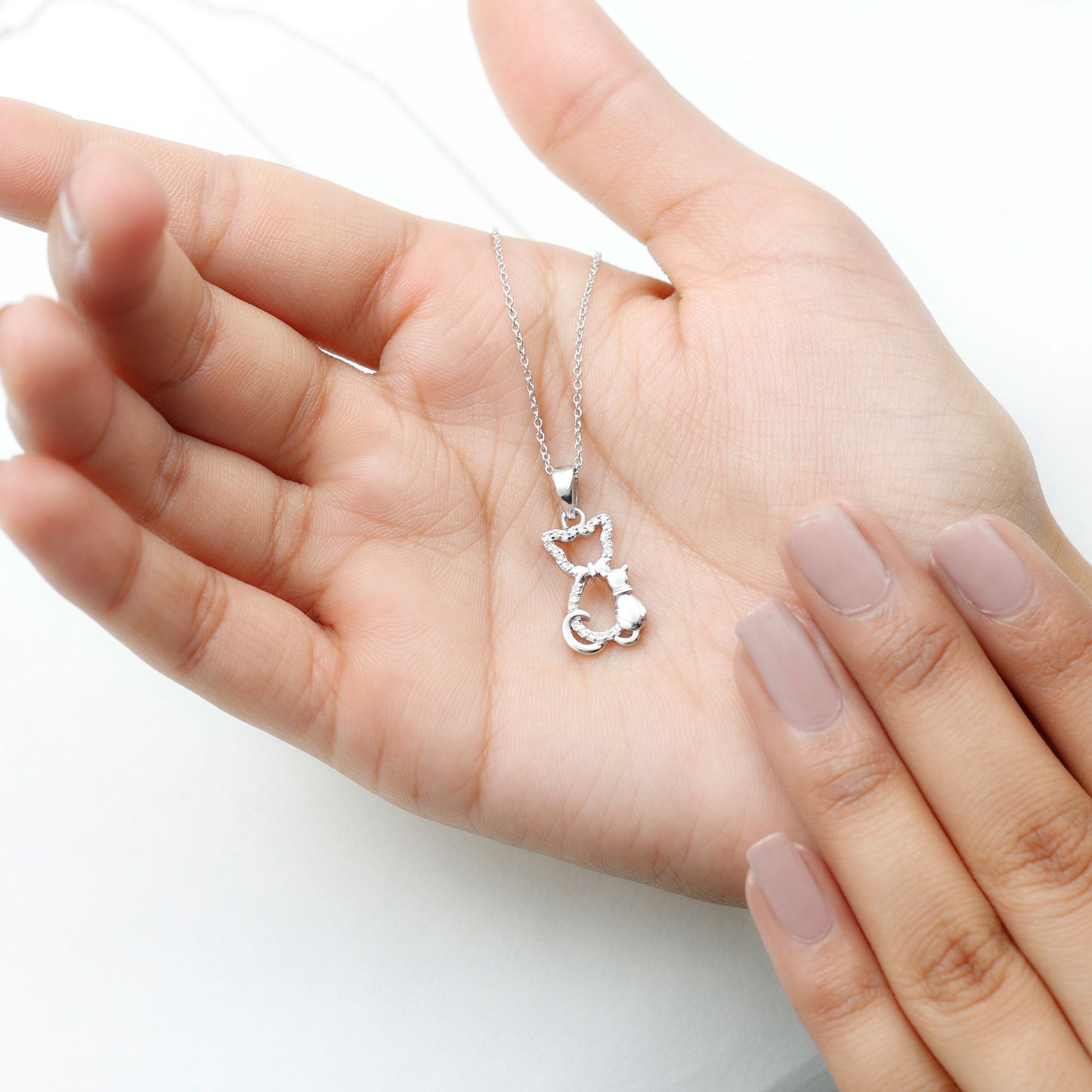 Silver cat-shaped pendant necklace held in a hand with light pink nail polish on a white background Kitty Cat Necklace, Cat Pendant, Cat Lover Gift, Diamond Necklace, Diamond Pendant, Lab Diamond Necklace, Natural Diamond Necklace, Fine Jewelry, Luxury Jewelry, Sterling Silver Necklace, 10K Gold Necklace, 14K Gold Necklace, 18K Gold Necklace, White Gold Necklace, Yellow Gold Necklace, Pendant Necklace, Cat Jewelry, Animal Jewelry, Women's Jewelry, Unisex Jewelry, Gift For Her, Luxury Gift, Birthday Gift, An