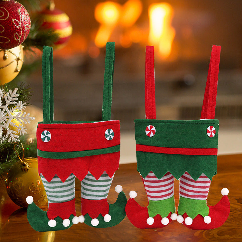 Two festive elf stocking gift bags with striped socks on a wooden surface, Christmas decorations in the background.
