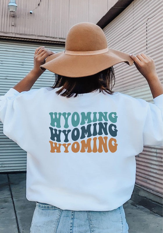 Person wearing a white sweatshirt with 'Wyoming' printed multiple times, holding a brown hat.