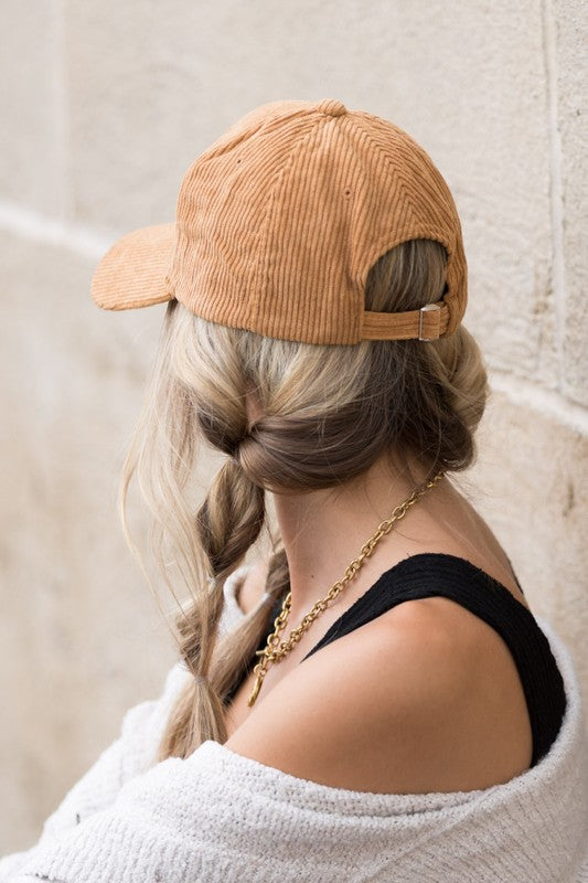 Woman wearing a brown corduroy boyfriend baseball cap with a relaxed fit, paired with a neutral sweater against a beige wall.