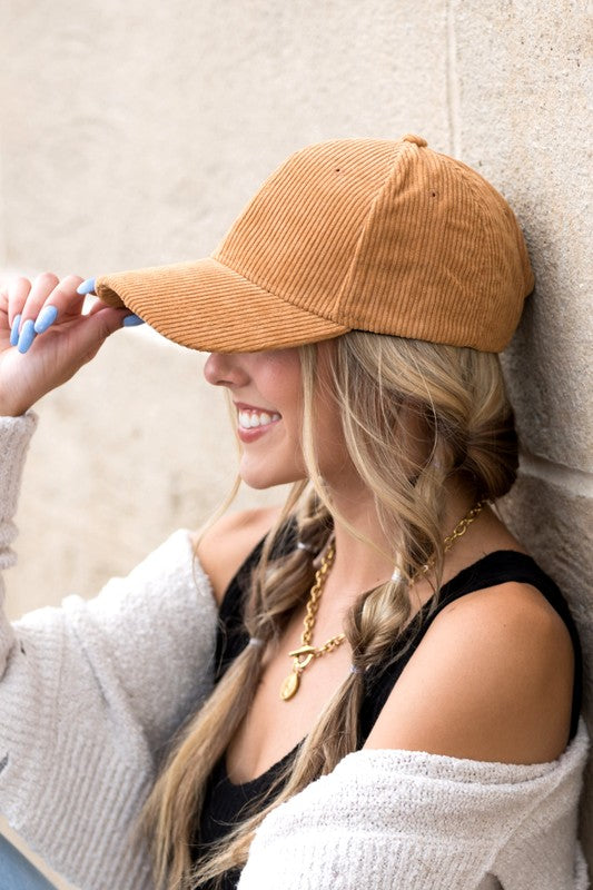 Woman wearing a brown corduroy cap against a beige wall