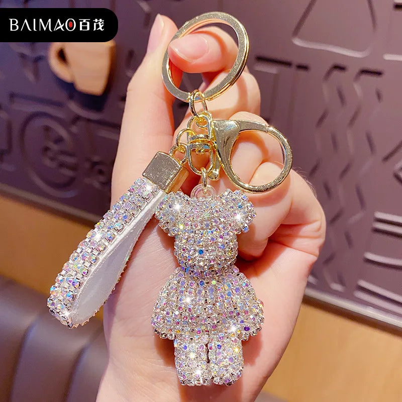 Sparkling rhinestone teddy bear keychain with a matching tassel, gold-tone hardware, and key ring, displayed in a hand. Decorative bag charm for purses, backpacks, keys, and car accessories. Brand watermark visible in the image.