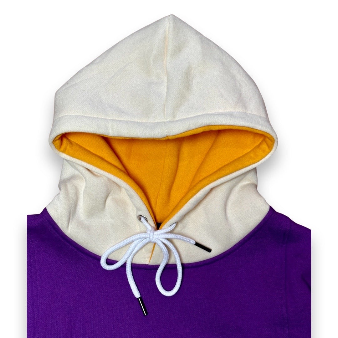 A close-up of a hooded sweatshirt showing a cream-colored hood lining with a bright yellow-orange interior, a white drawstring, and a purple body, photographed on a white background.