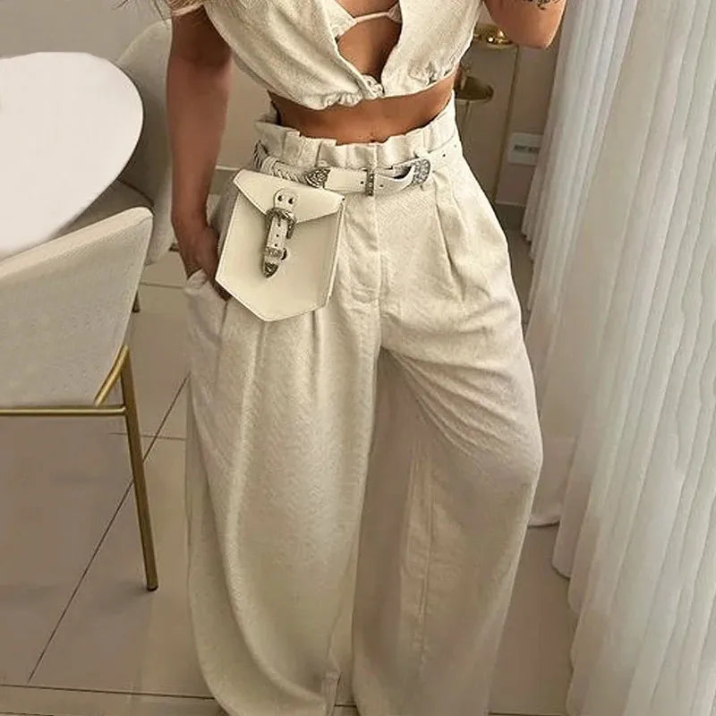 Women's cream two-piece outfit with sleeveless cropped top, high-waisted wide leg pants, statement belt, matching mini handbag, elegant monochrome co-ord set for summer vacation, resort wear, casual chic fashion, boutique women's clothing, modern street style outfit.
