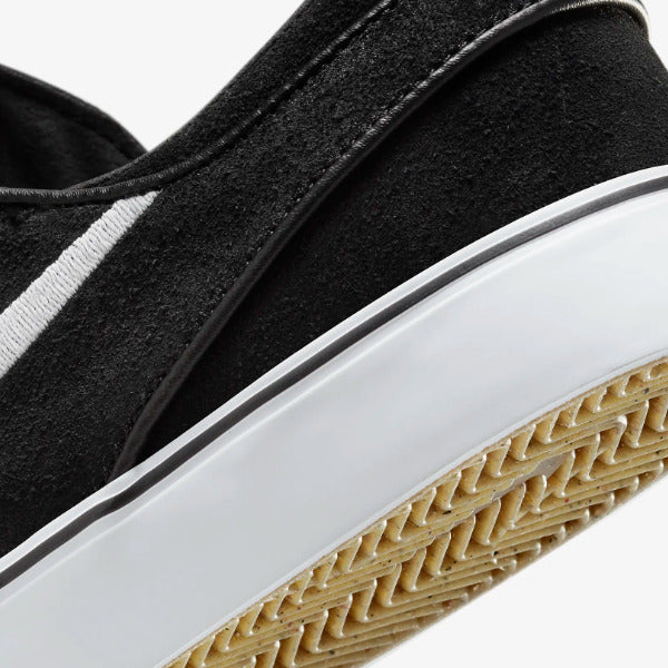 Close-up of a black suede slip-on shoe with a white midsole and a tan textured outsole, shown against a light gray background. Nike SB Janoski Black White