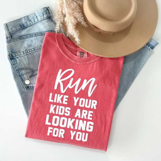 A red unisex graphic tee featuring humorous text, styled with denim shorts and a hat, displayed on a clean white background.