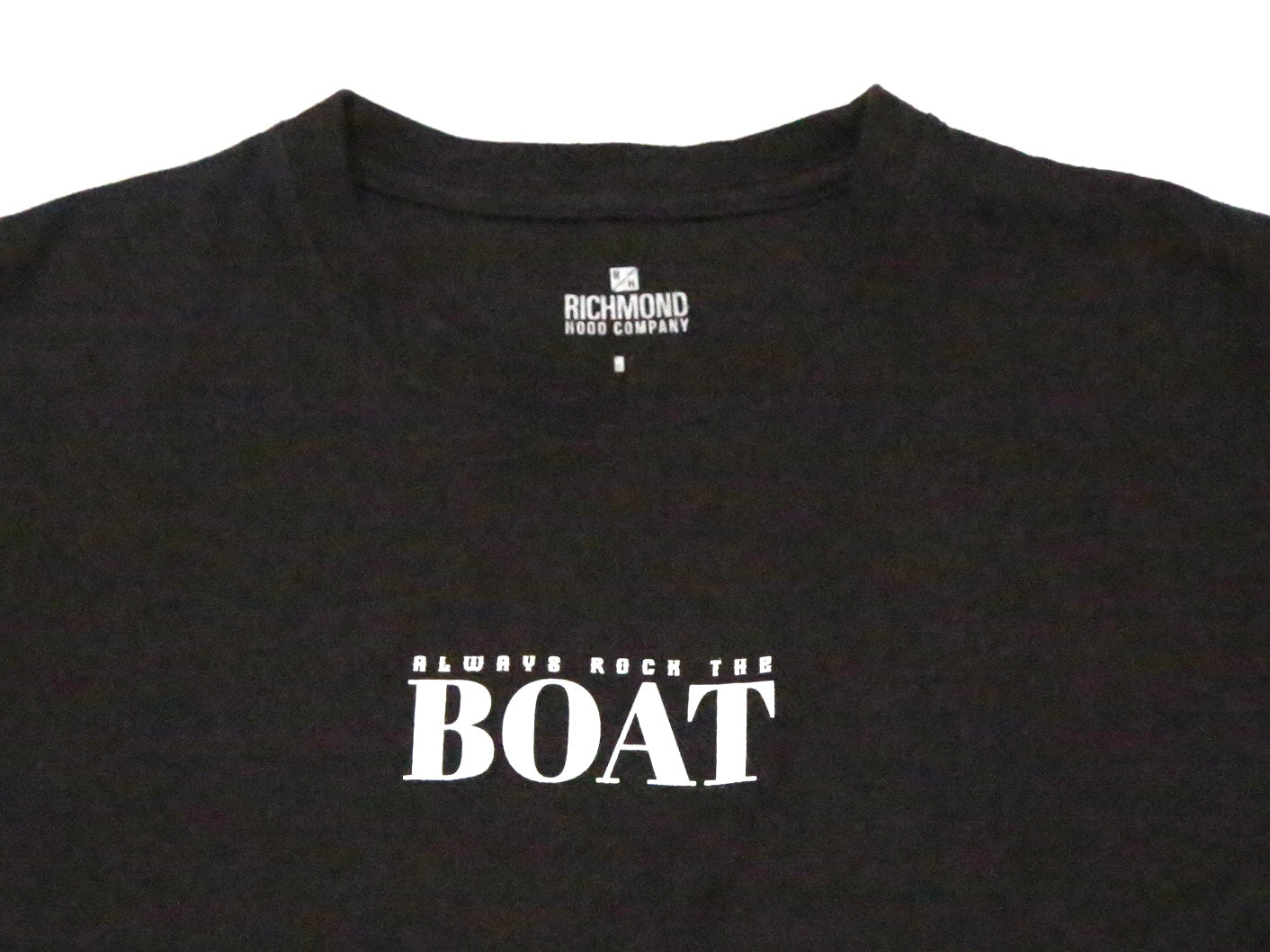 A close-up of a black Richmond News Company t-shirt featuring the slogan 'ALWAYS ROCK THE BOAT' printed in white on the chest.