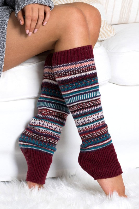 Woman wearing multicolor Fair Isle knit leg warmers featuring a classic Nordic-inspired pattern in red, gray, navy, and cream tones. These soft acrylic leg warmers showcase a thick ribbed cuff and cozy textured knit construction, providing warmth and comfort for cold-weather styling. Perfect for pairing with boots, leggings, jeans, tights, and winter outfits, these fashionable leg warmers add a rustic cabin-chic touch to everyday wear. Ideal for fall and winter fashion, holiday outfits, ski lodge getaways, 
