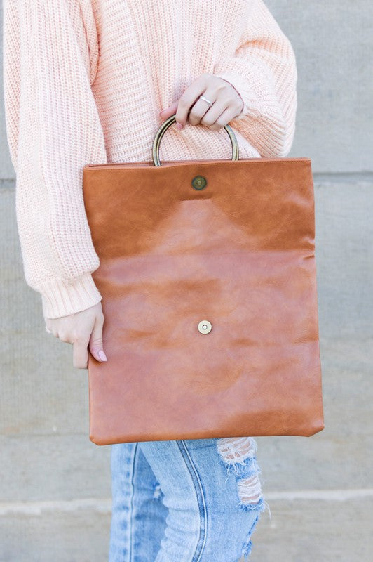 Women's cognac brown fold-over clutch purse with antique bronze O-ring handle, spacious expandable interior, and soft faux leather construction. Elegant envelope-style handbag featuring a magnetic snap closure and versatile fold-over design, perfect for work, travel, shopping, brunch, weddings, evening events, date nights, and everyday wear. Designer-inspired cognac clutch bag blending timeless sophistication, practicality, and modern style.