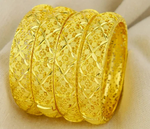 Four gold bangles with intricate designs on a beige fabric background