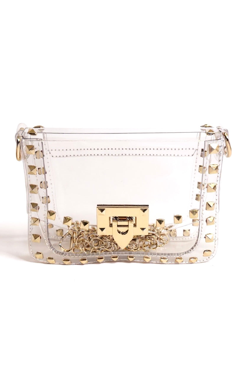 A clear vinyl shoulder bag with gold-tone studs, a gold chain strap, and a gold turn-lock clasp, photographed on a white background.