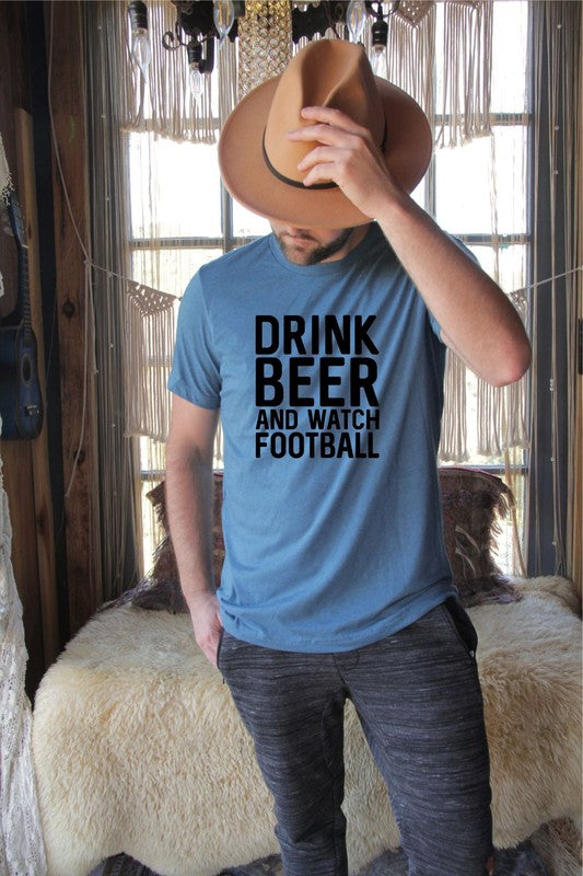 Man wearing a blue graphic t-shirt featuring the bold slogan “Drink Beer and Watch Football” in large black lettering. This premium unisex ring-spun cotton tee combines casual comfort with sports fan style, making it perfect for football season, tailgates, game day parties, sports bars, weekend gatherings, and everyday wear. Styled with dark jeans beside a vintage motorcycle, this soft cotton graphic shirt is an ideal gift for football fans, beer enthusiasts, sports lovers, husbands, boyfriends, dads, and 