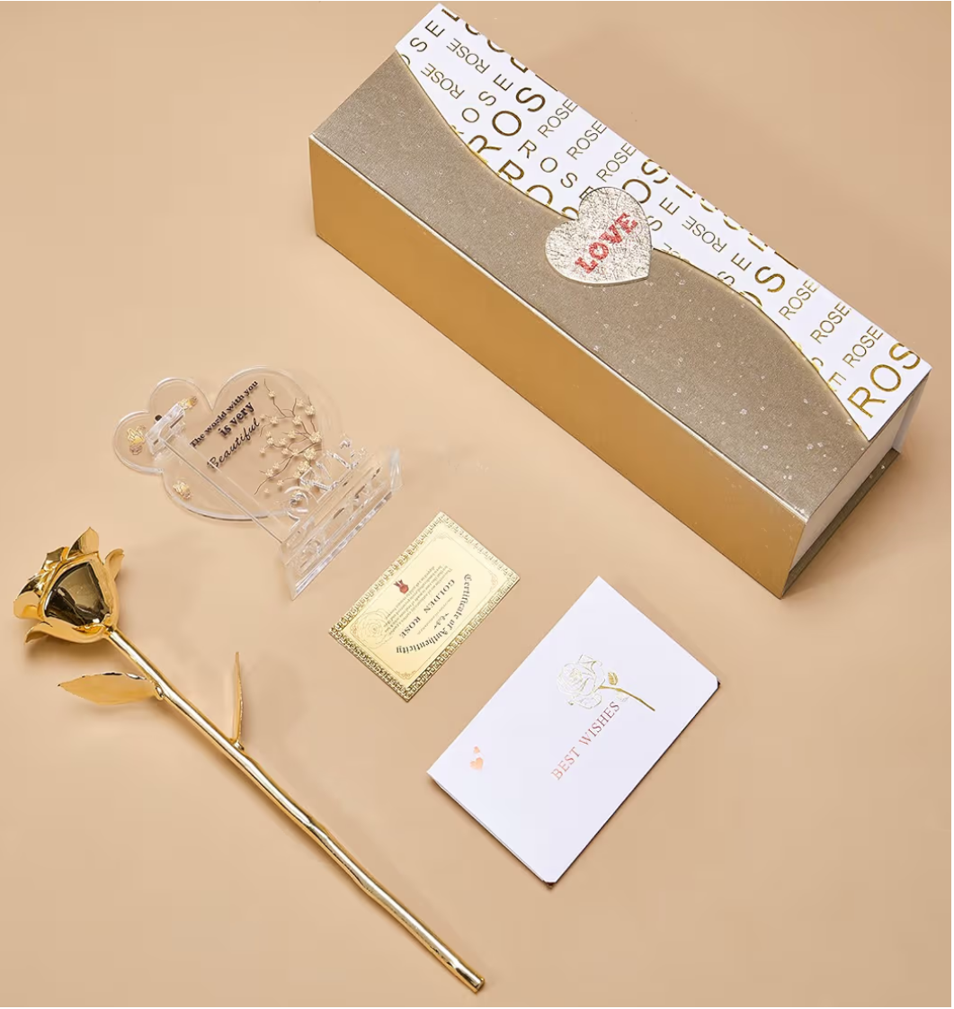 Gold rose-shaped pen with decorative box, card, and clear heart-shaped object on a beige background