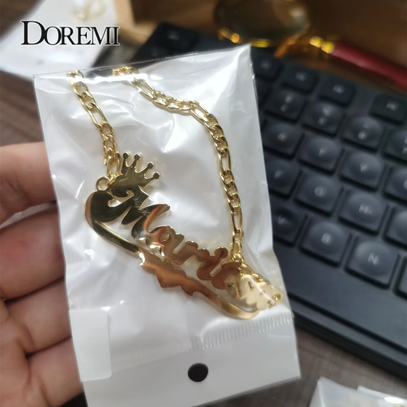 Customized Gold necklace with pendant held by a hand, against a blurred keyboard background.