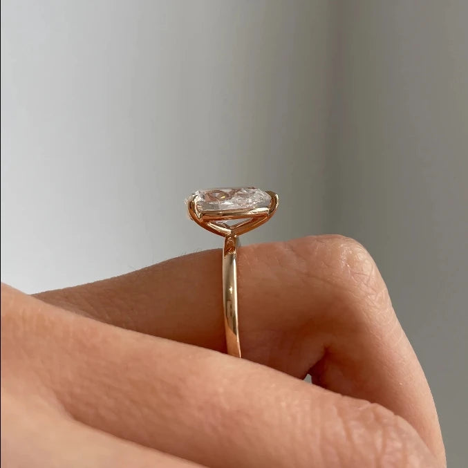 Rose gold ring with a diamond held in a hand against a neutral background