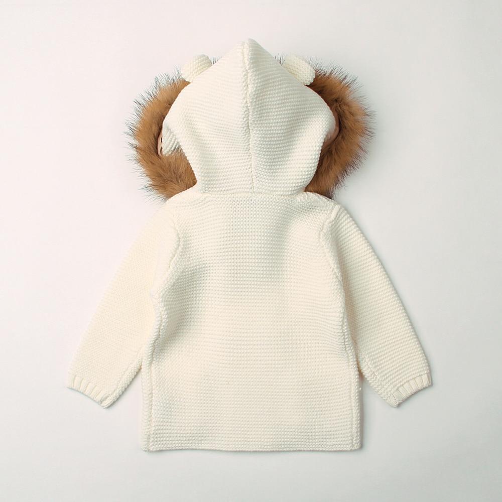 White knitted hoodie with brown fur trim on a light gray background