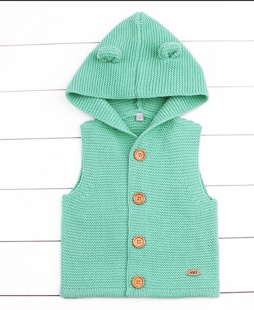 Green knitted vest with a hood on a white wooden background