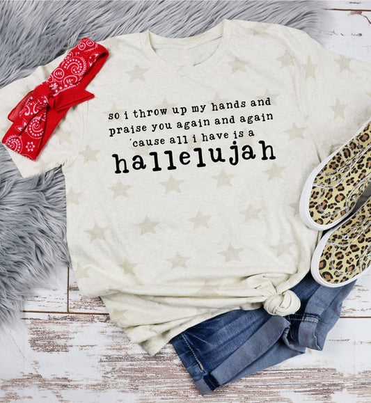 White t-shirt with text, red bandana, leopard print item, and jeans on a wooden surface. Cream flat lay graphic T-shirt featuring the inspirational phrase, "so I throw up my hands and praise you again and again 'cause all I have is a hallelujah," styled with a red bandana, cuffed blue jeans, and leopard print slip-on shoes on a rustic white wooden background.