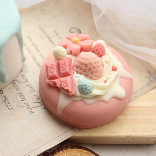Pink dessert-shaped soap with strawberries and chocolate decorations on a wooden surface.