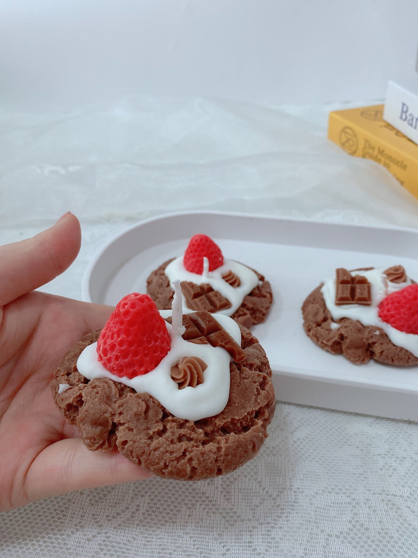 Chocolate cookies with white icing and raspberries held by a hand, with a tray of similar cookies in the background. Chocolate desserts with whipped cream and raspberries on a white tablecloth. Handmade Strawberry Cake Aromatic Candle Decoration. Chocolate cookies with whipped cream and raspberries on a white plate. Indulge your senses with this delightful handmade strawberry cake aromatic candle! Crafted from eco-friendly soybean wax, this charming sector-shaped beauty fills your space with a sweet, bakery