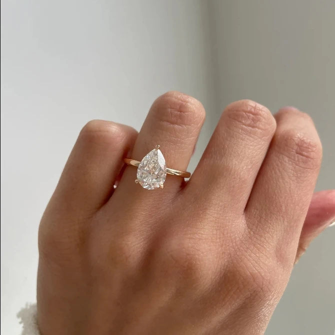 Rose gold ring with a pear-shaped diamond on a hand against a neutral background