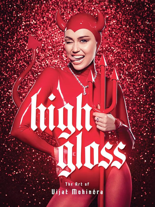 A book cover photo of Miley Cyrus smiling woman in a red devil costume with horns, a tail, and a trident stands against a sparkling red background. Large white gothic text across the center reads 'high gloss', with smaller text below reading 'The Art of Vijat Mohindra'.
