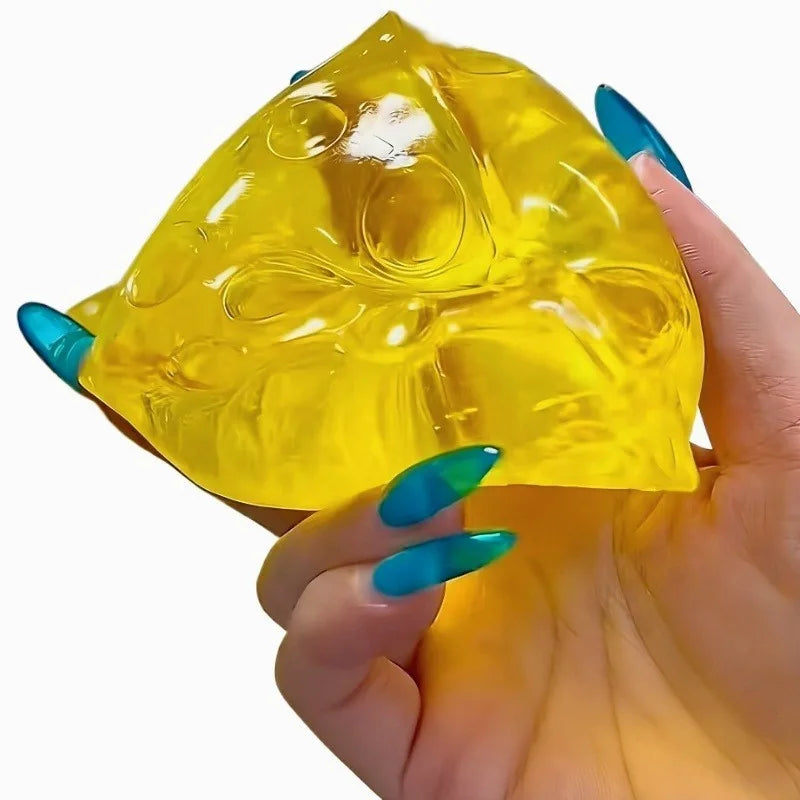 Hand holding a translucent yellow honey cheese squishy toy shaped like a cheese wedge, a soft mochi stress relief squeeze cube for anxiety relief and sensory fidget play, shown against a white background with blue acrylic nails. Squishy Toy