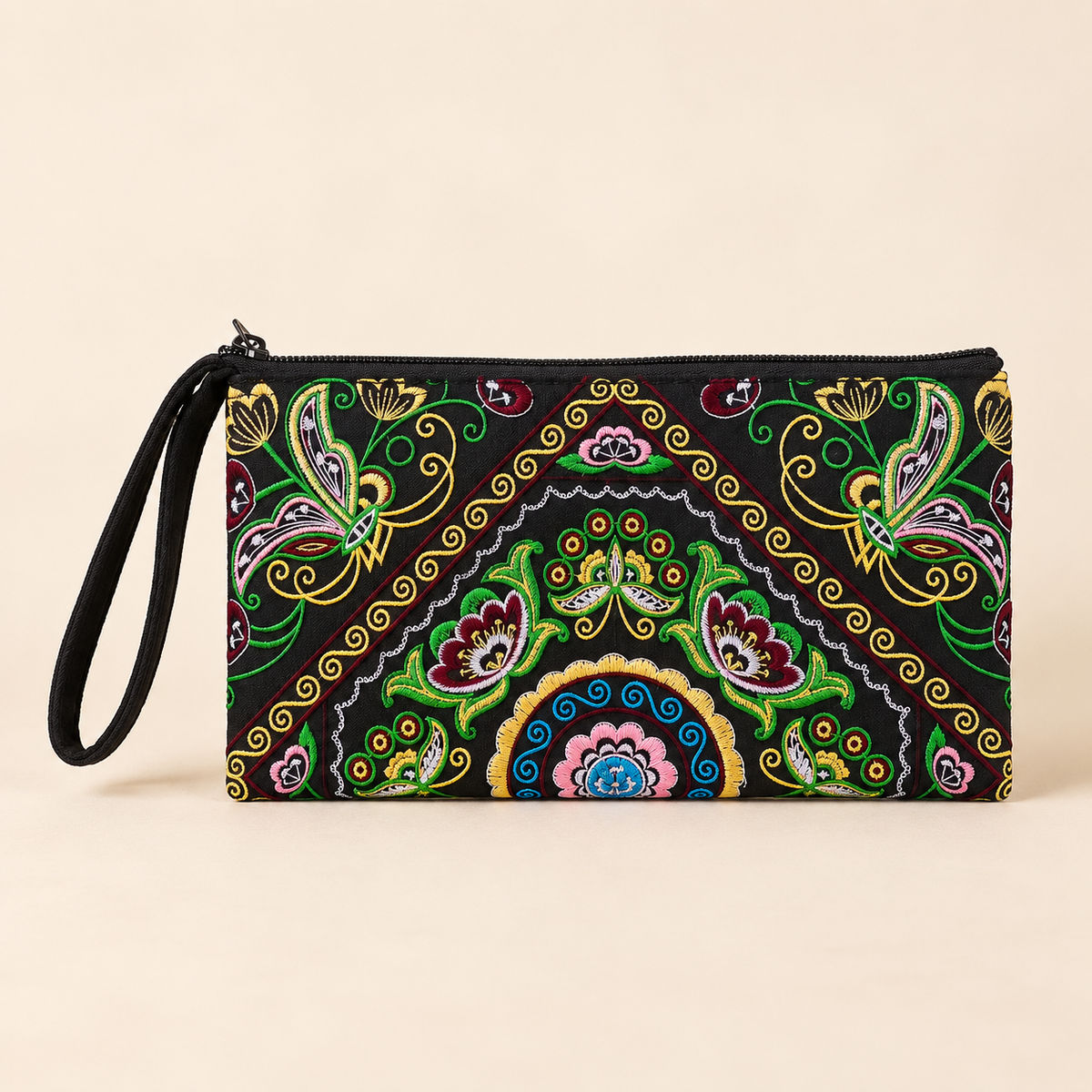 A rectangular wristlet clutch with a black zipper and attached black wrist strap, featuring a vibrant, multicolored traditional folk art pattern on a black background, set against a solid beige backdrop.
