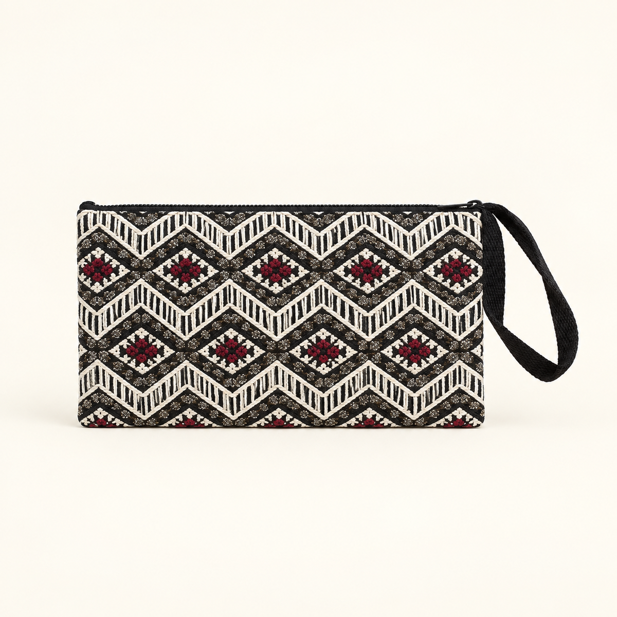 A rectangular wristlet clutch with a black and white geometric ikat pattern and red starburst accents, featuring a black wrist strap on a light cream background.