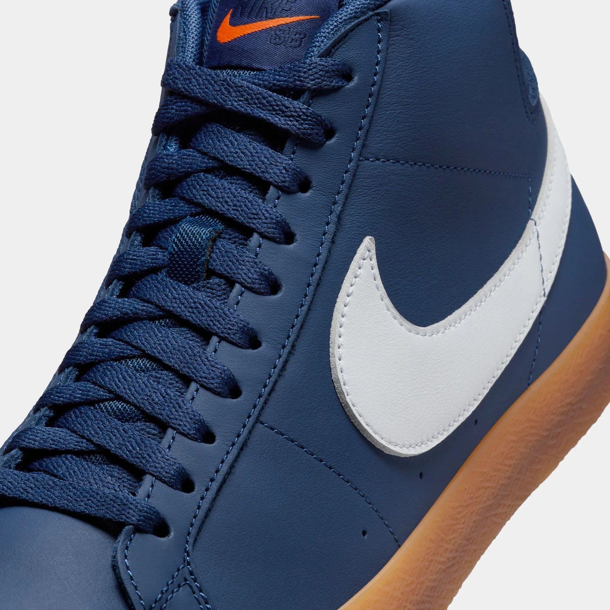 Close-up of a Nike high-top sneaker in navy blue with a white Swoosh, navy laces, and a gum brown outsole, shown against a light gray background.