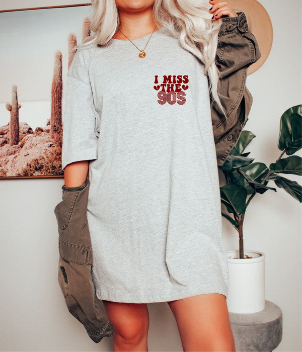 Woman wearing a heather gray "I Miss The 90s" graphic softstyle t-shirt featuring vintage retro lettering on the left chest, styled with a casual oversized jacket for a nostalgic 90s-inspired look.