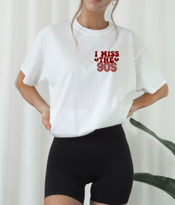 Woman wearing a white softstyle graphic T-shirt featuring a vintage red "I Miss The 90s" left chest print, styled with black biker shorts for a casual retro-inspired look.