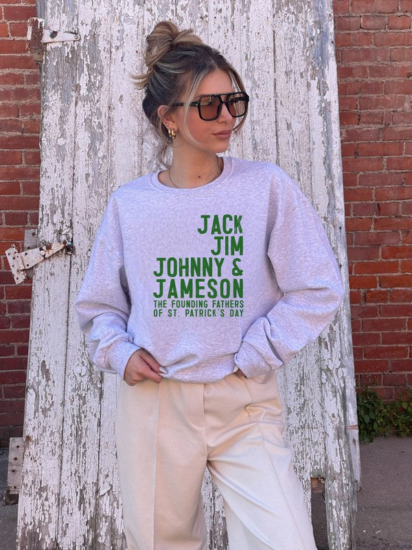 Woman wearing an Oxford grey plus size St. Patrick's Day graphic sweatshirt with green "Jack Jim Johnny & Jameson – The Founding Fathers of St. Patrick's Day" design, styled with cream pants and oversized sunglasses against a rustic wooden door backdrop.