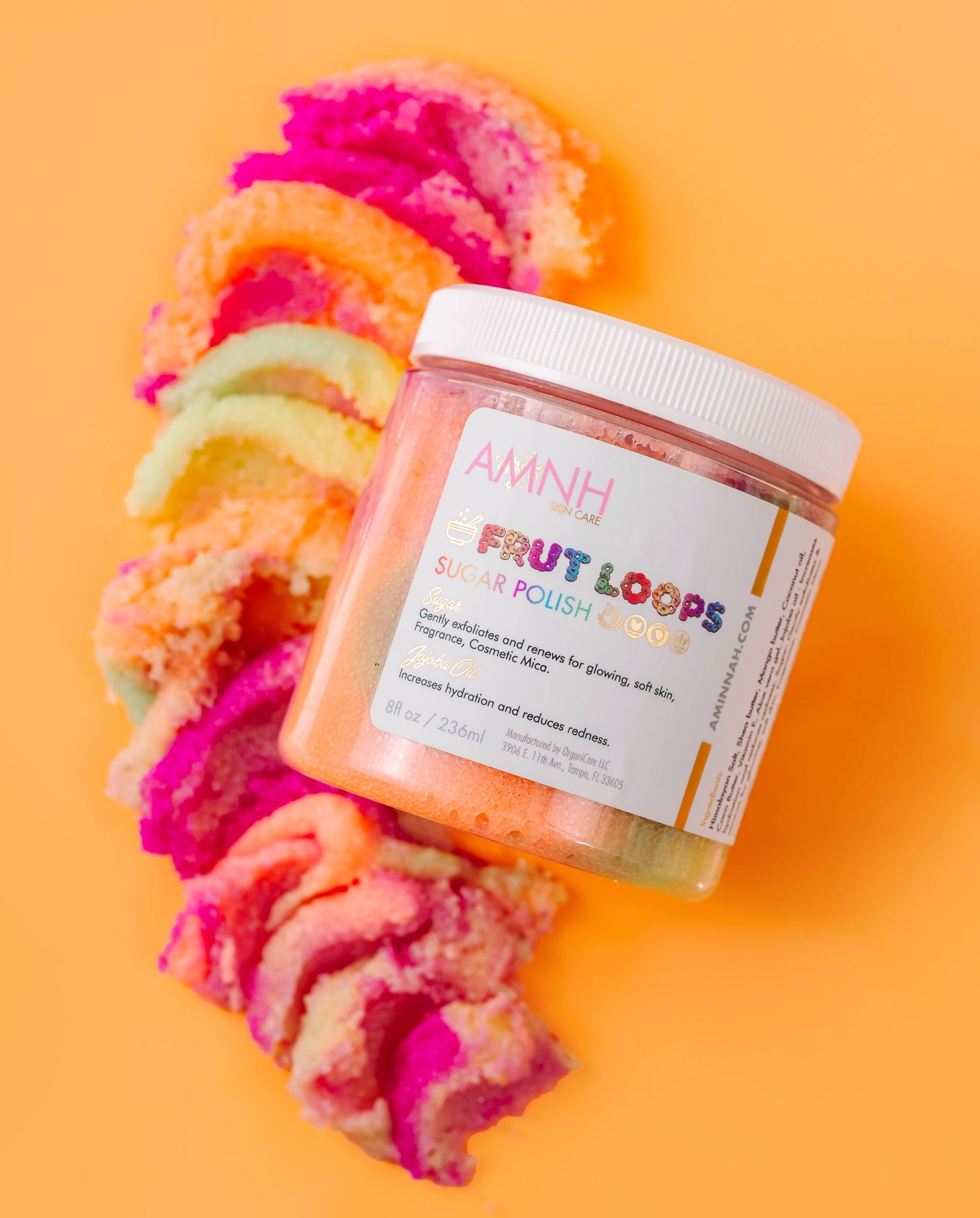 Jar of 'Fruit Loops' body sugar scrub product with colorful hair on an orange background