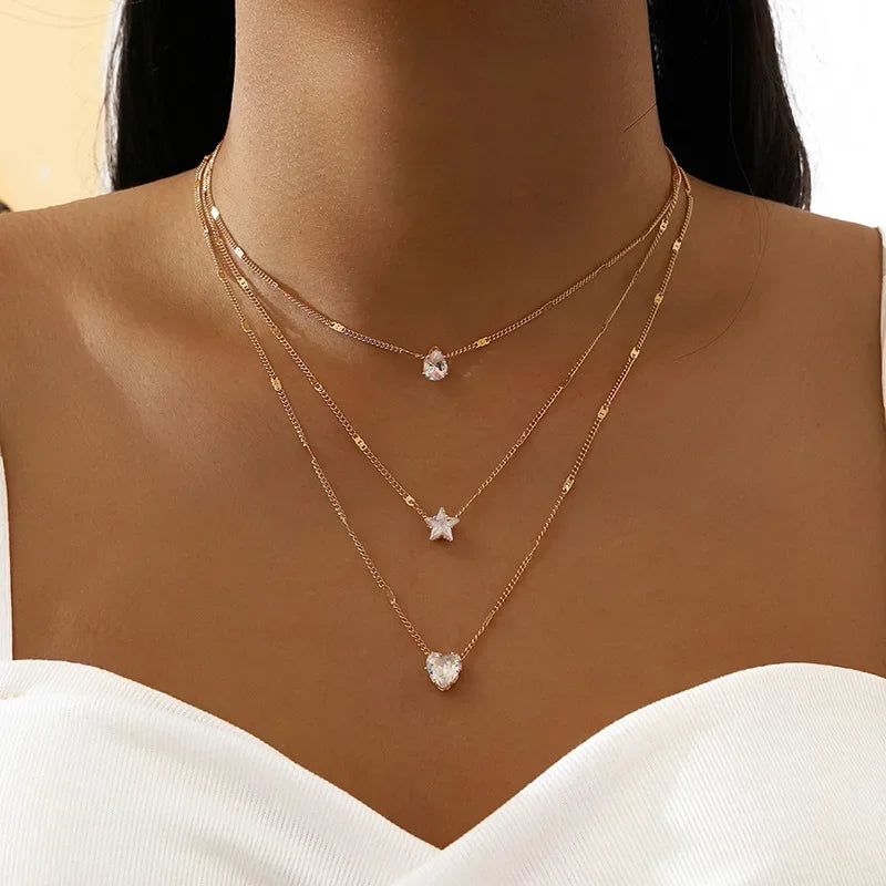 Layered gold necklaces with heart and star pendants on a model wearing a white top.