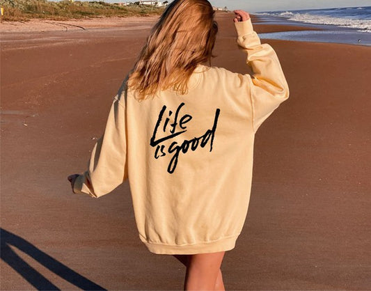 Person wearing a 'Life is good' sweatshirt on a beach