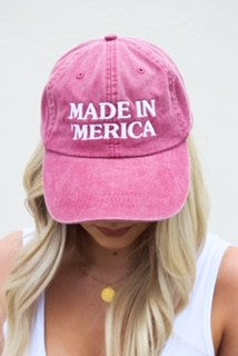 Pink cap with 'MADE IN MERICA' text worn by a person with blonde hair.