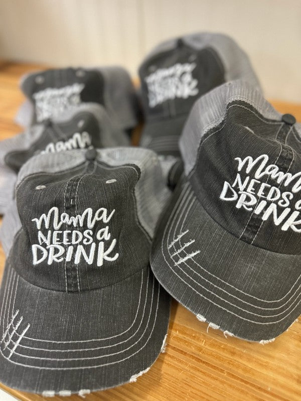 Gray hats with 'Mama Needs a Drink' text on a wooden surface. Mama Needs a Drink Embroidered Trucker Hat – Funny Mom Mesh Baseball Cap | Adjustable Snapback Hat for Mothers